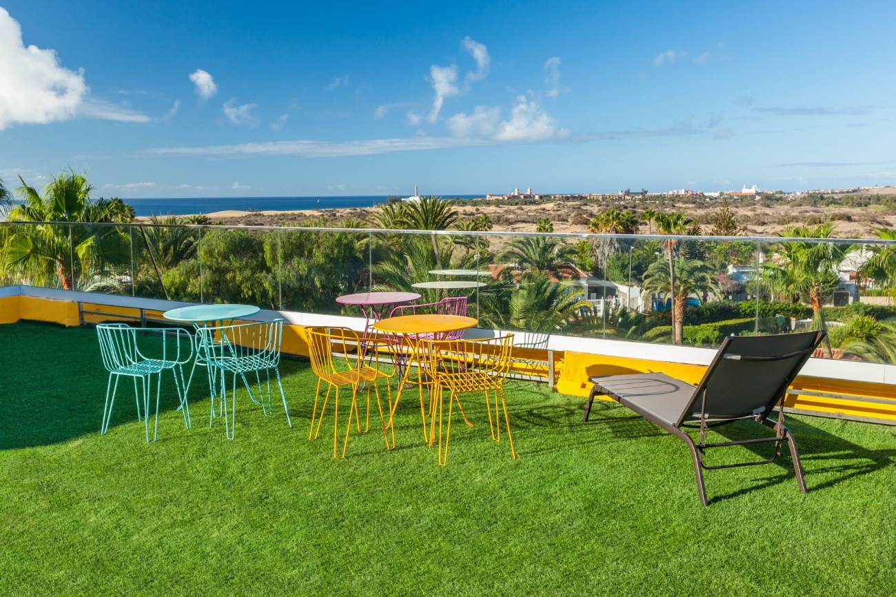 Terraza con césped y mesas de colores, con vistas a las dunas de Maspalomas y al mar
