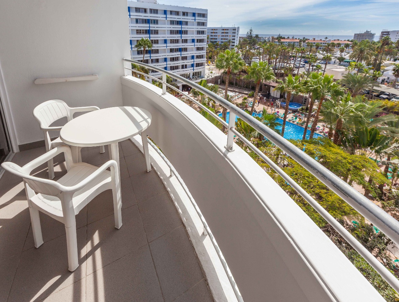 Balcón con mesa y sillas sobre los jardines y la piscina